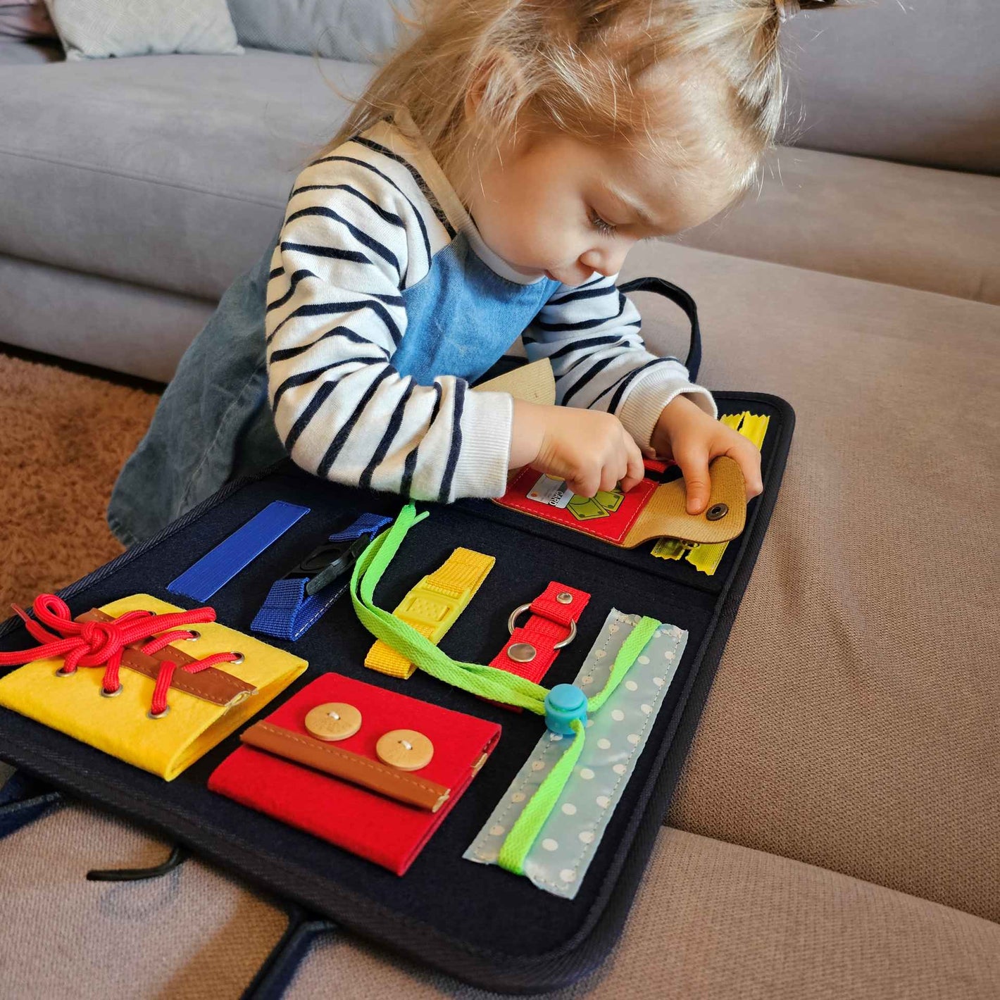 Ein Kind spielt konzentriert mit einem sensorischen Buch, das verschiedene Verschlüsse bietet, um feinmotorische Fähigkeiten zu fördern. Ideal für pädagogische Inhalte, die die Bedeutung von spielerischem Lernen hervorheben.