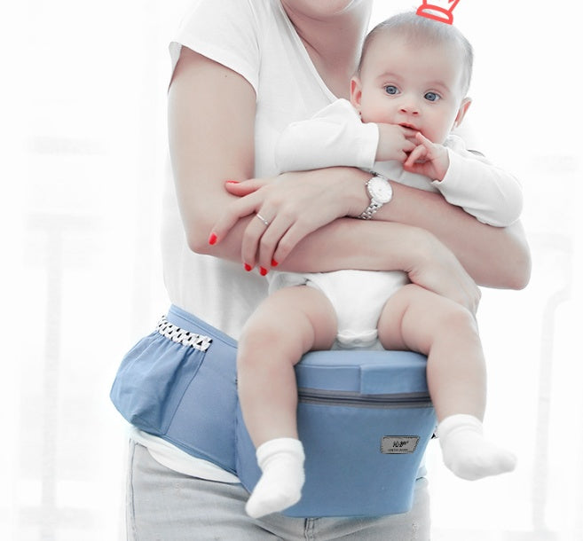 Eine junge Mutter in einem weißen T-Shirt hält ein Baby, das in einen weißen Strampler gekleidet ist und eine kleine rote Schleife auf dem Kopf trägt. Das Baby sitzt in einer blauen Hüfttrage, die um die Taille der Frau befestigt ist und das Gewicht des Babys unterstützt.