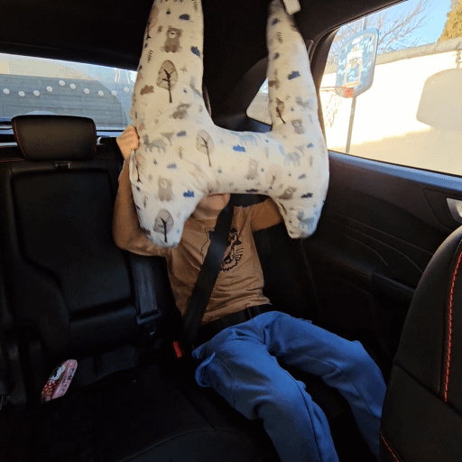 Junges Kind schläft im Autositz, angelehnt an ein großes, gemustertes Nackenkissen. Gut geeignet für Themen rund um Reisen mit Kindern und Sicherheit im Straßenverkehr. Das GIF zeigt wie einfach das kissen anzulegen ist.