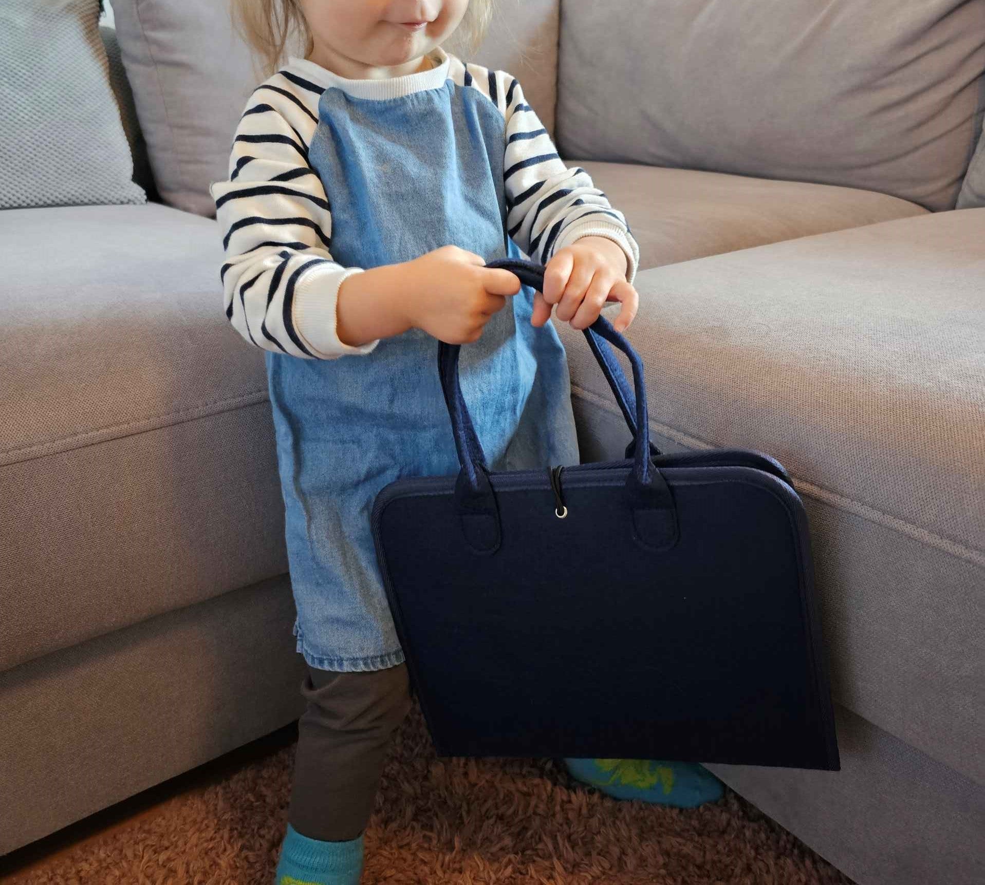Ein kleines Mädchen das voller stolz ihren Lernkoffer in den Händen hält.